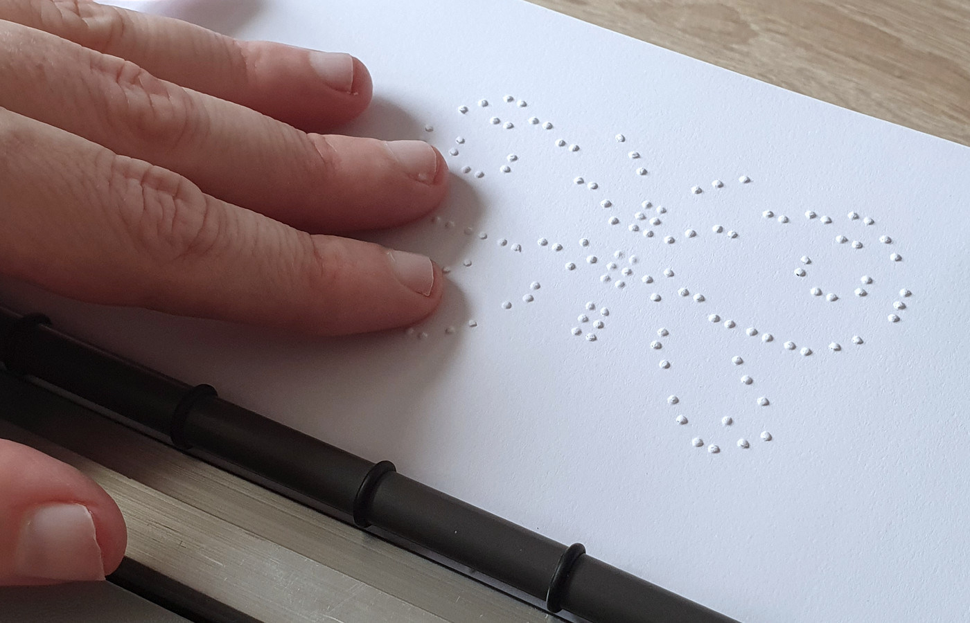 Eine Hand ertastet auf einem Blatt Papier das taktile Braillebild Schmetterling
